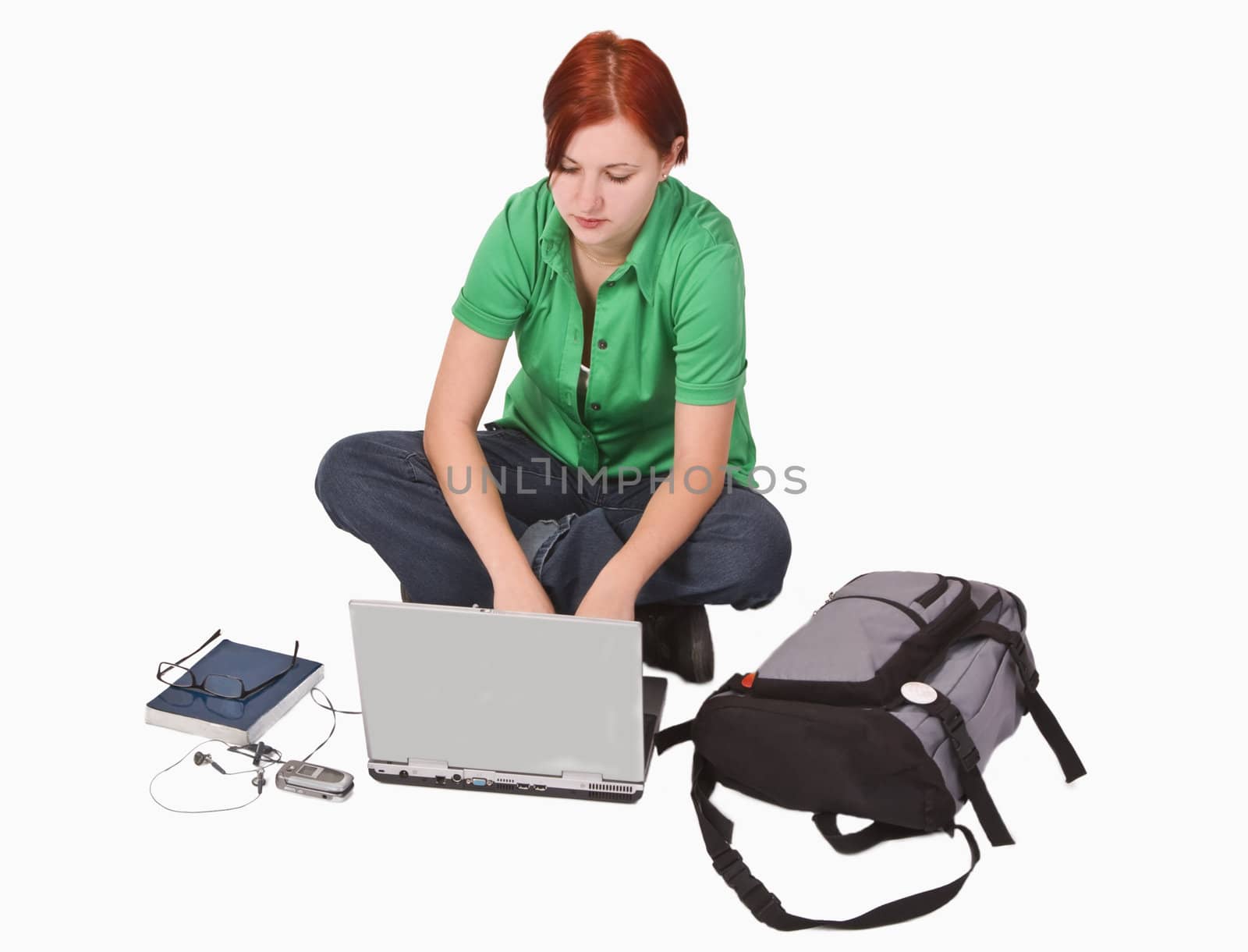 Redheaded teenage girl with a lot of items around her working on a laptop.