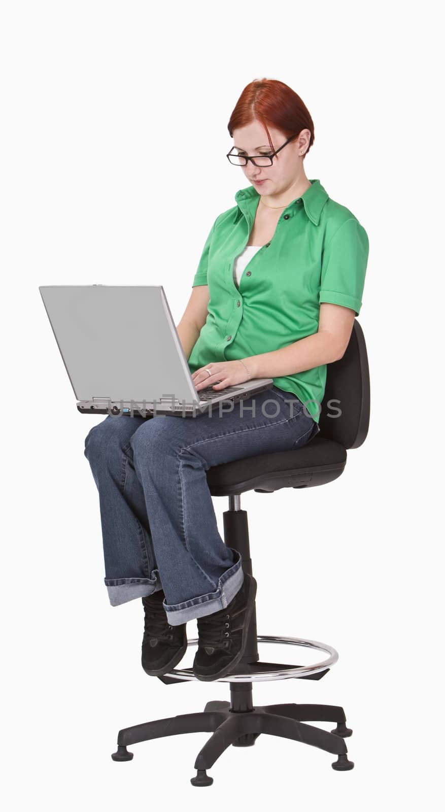 Redheaded teenager sitting on a high chair and working on a laptop.