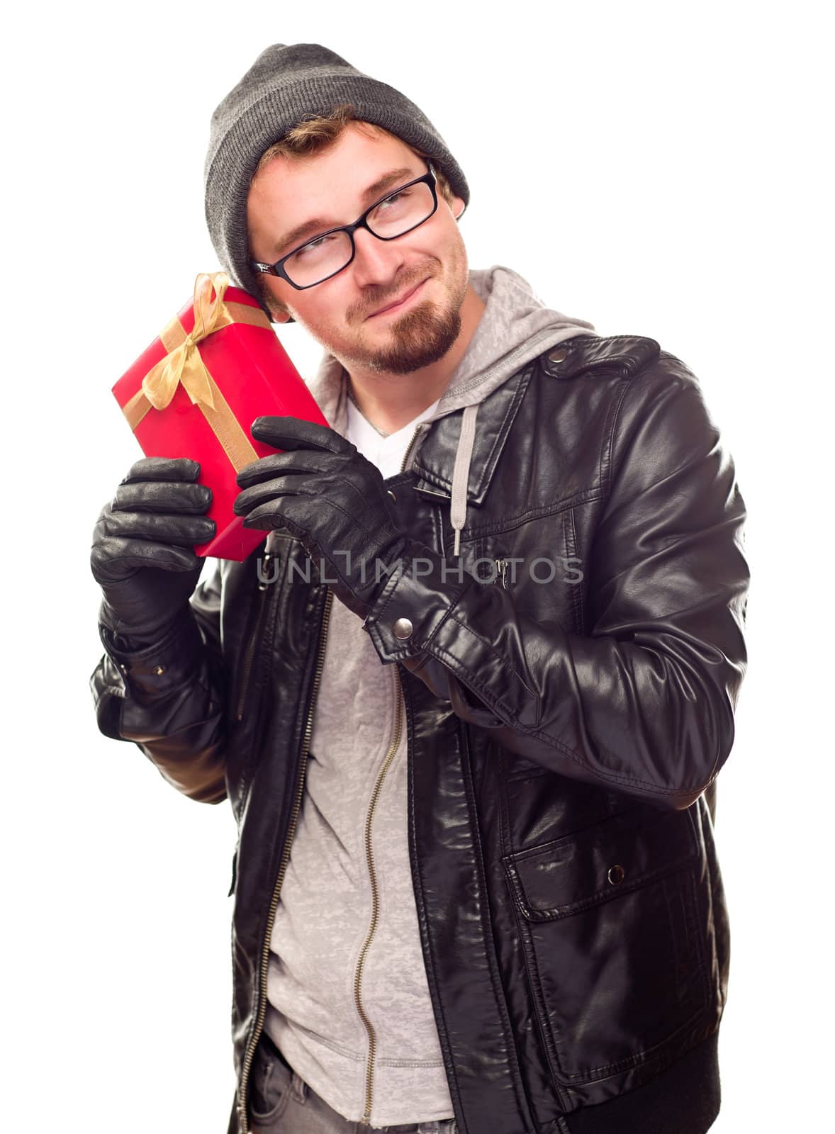 Warmly Dressed Handsome Young Man Holding Wrapped Gift To His Ear Isolated on a White Background.