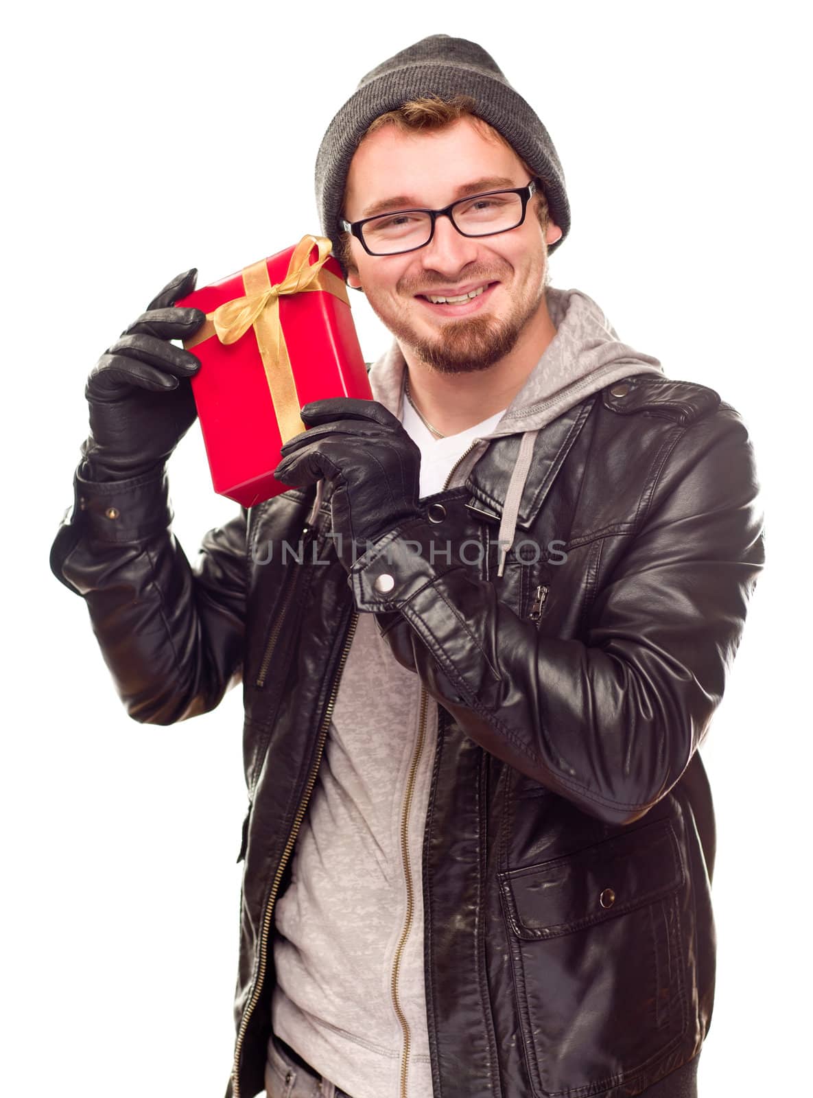 Warmly Dressed Handsome Young Man Holding Wrapped Gift To His Ear Isolated on a White Background.