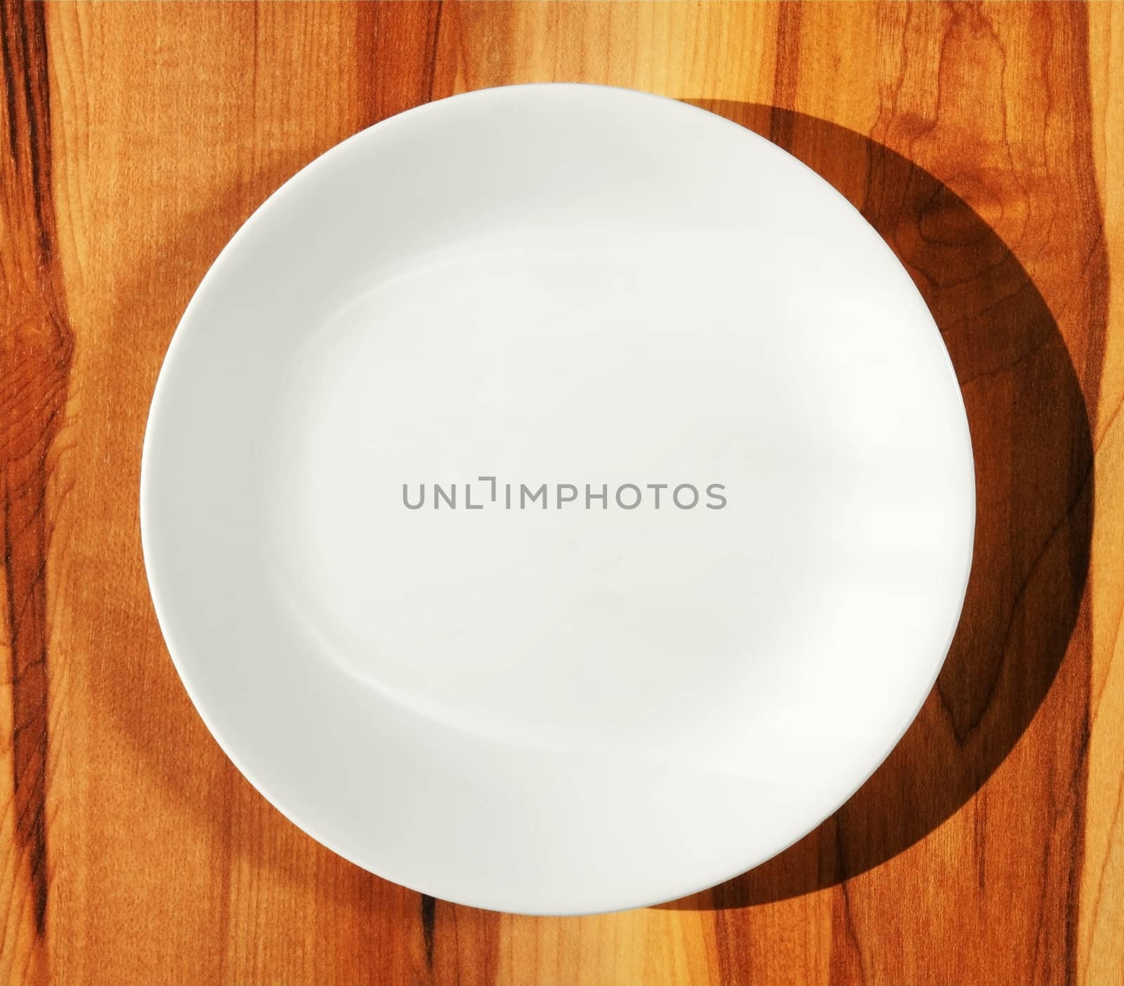 Pure white porcelain dinner plate on kitchen hard wood table with shadow.