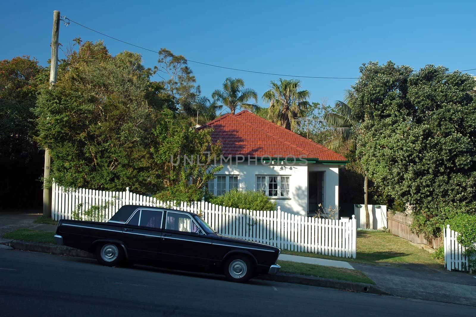 small white wooden house in suburb, black car parked in front