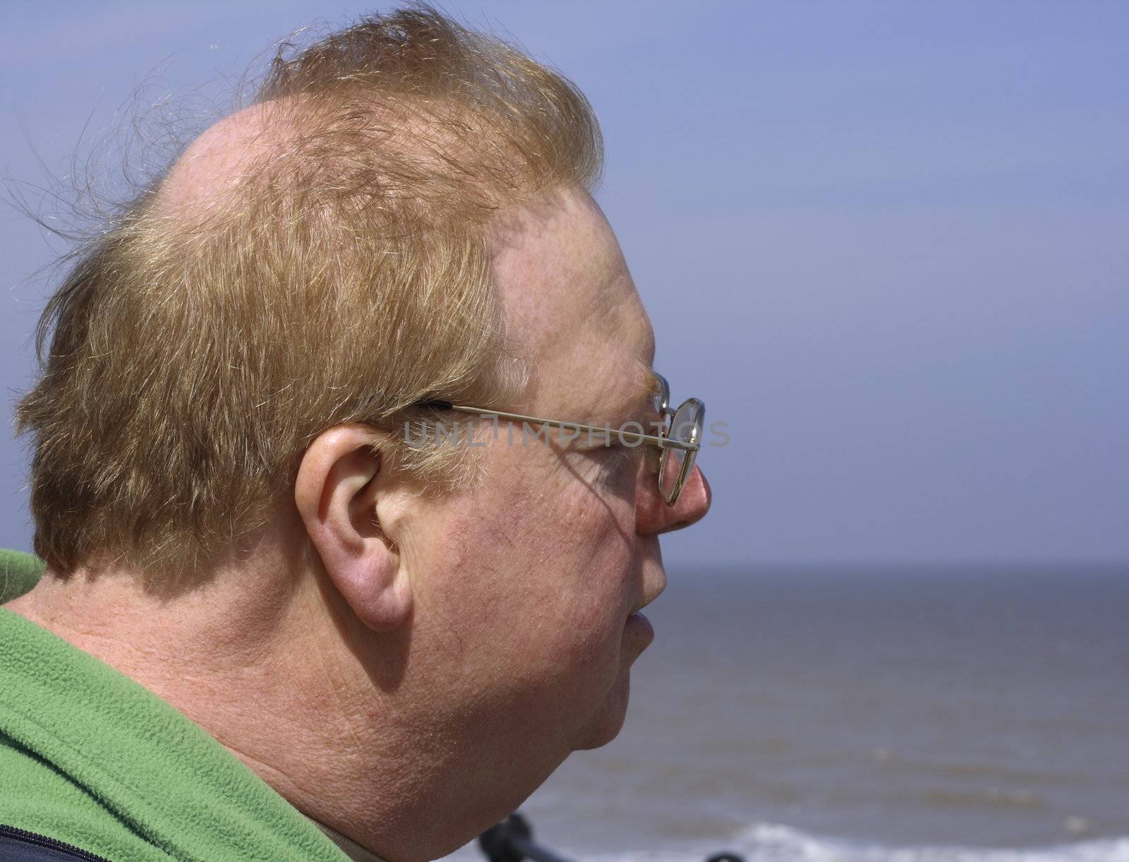 middle aged male with redhair and glasses looking out to sea