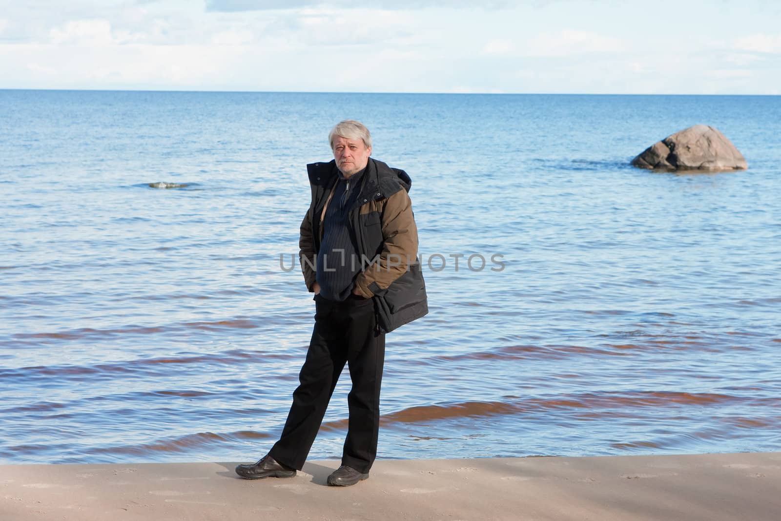 Mature man with grey hair relaxing at the Baltic sea in autumn day.