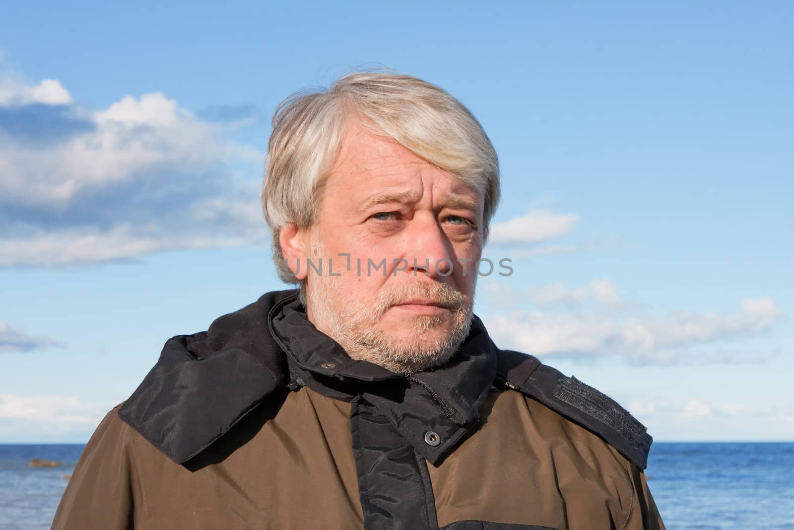 Portrait of mature concerned man with grey hair at the Baltic sea in autumn day.
