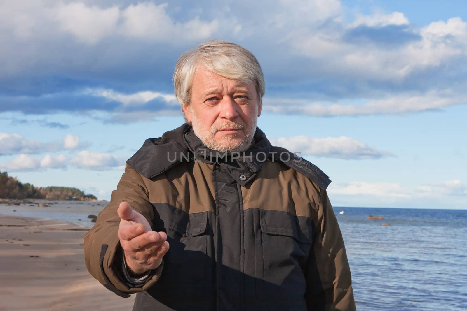 Mature poor man with grey hair at the Baltic sea asks for help in autumn day.