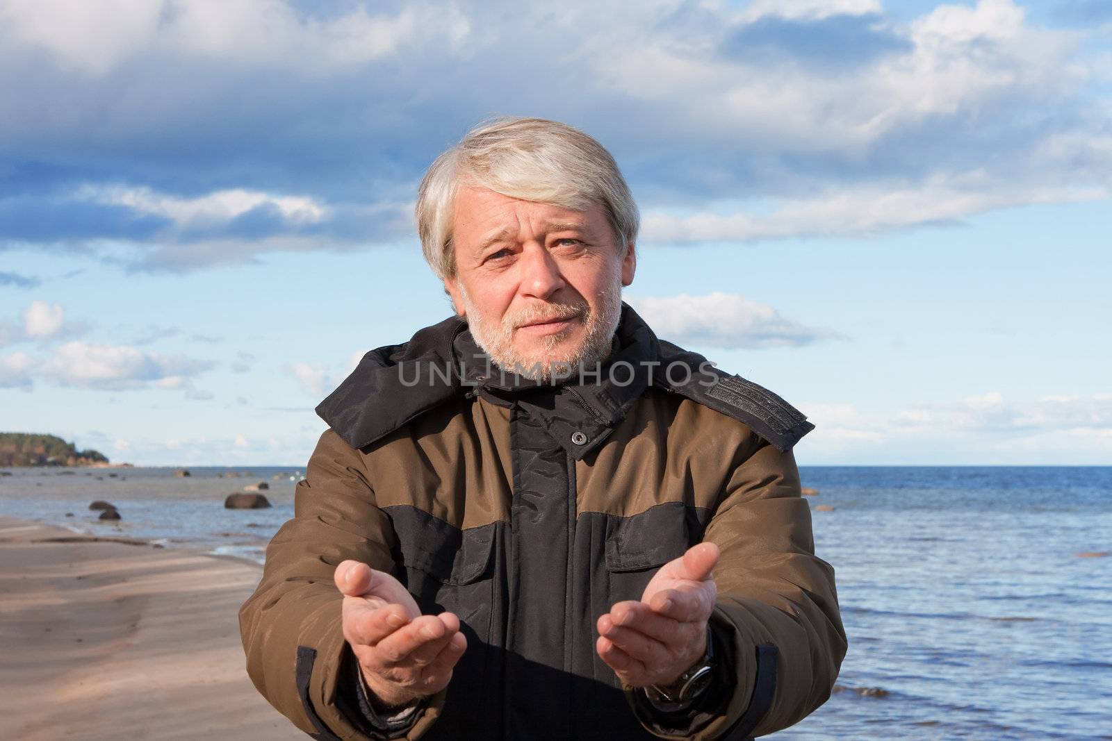 Mature poor man with grey hair at the Baltic sea asks for help in autumn day.