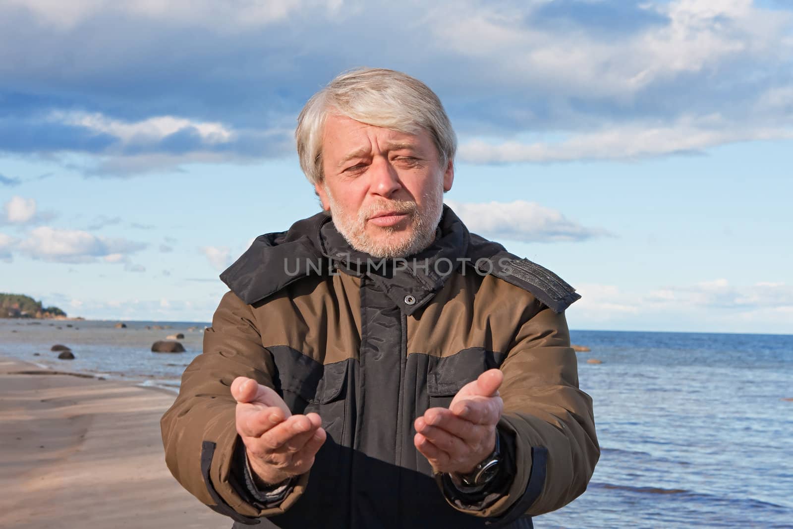 Mature poor man with grey hair at the Baltic sea asks for help in autumn day.