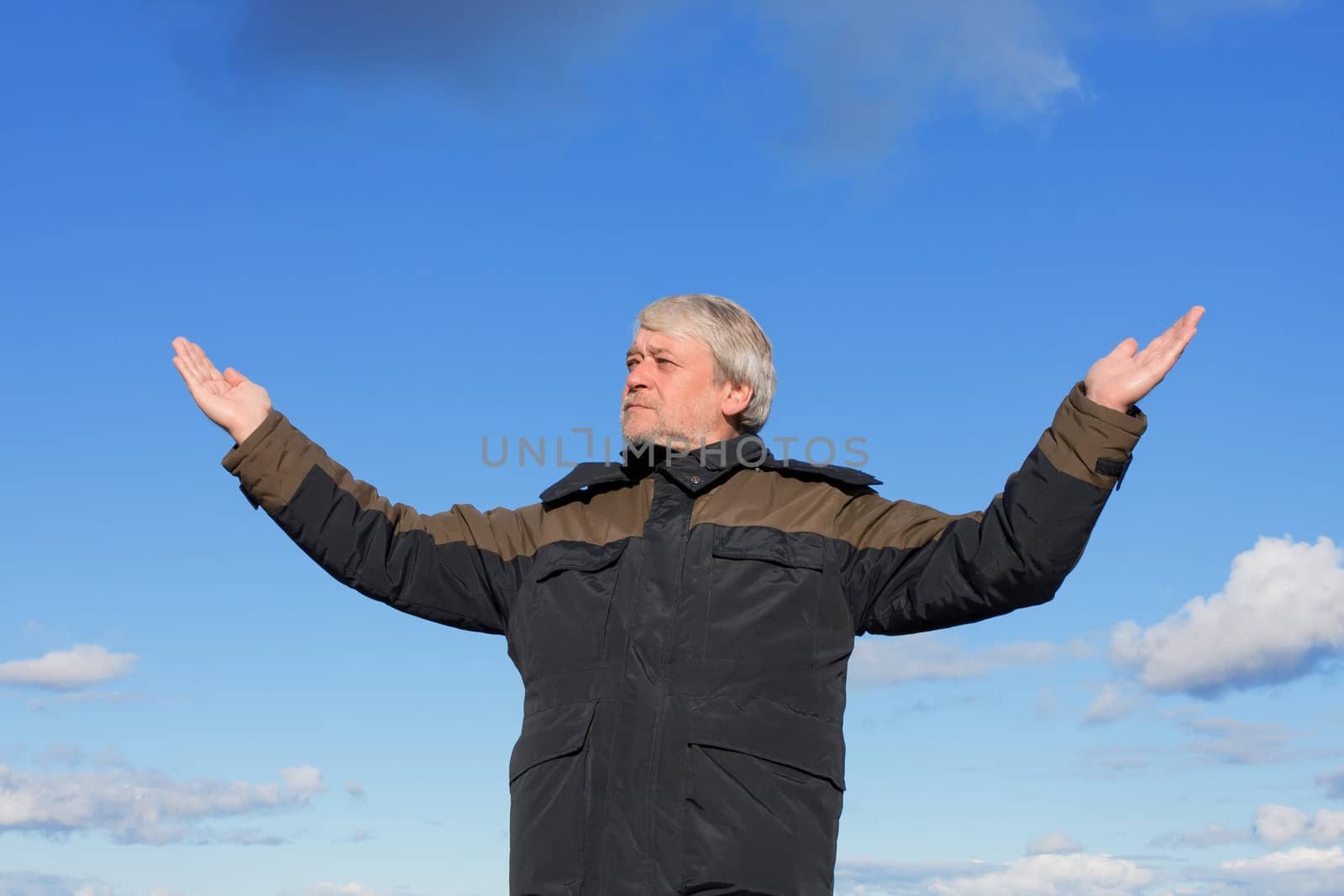 Mature man with grey hair relaxing on the blue sky of the background.