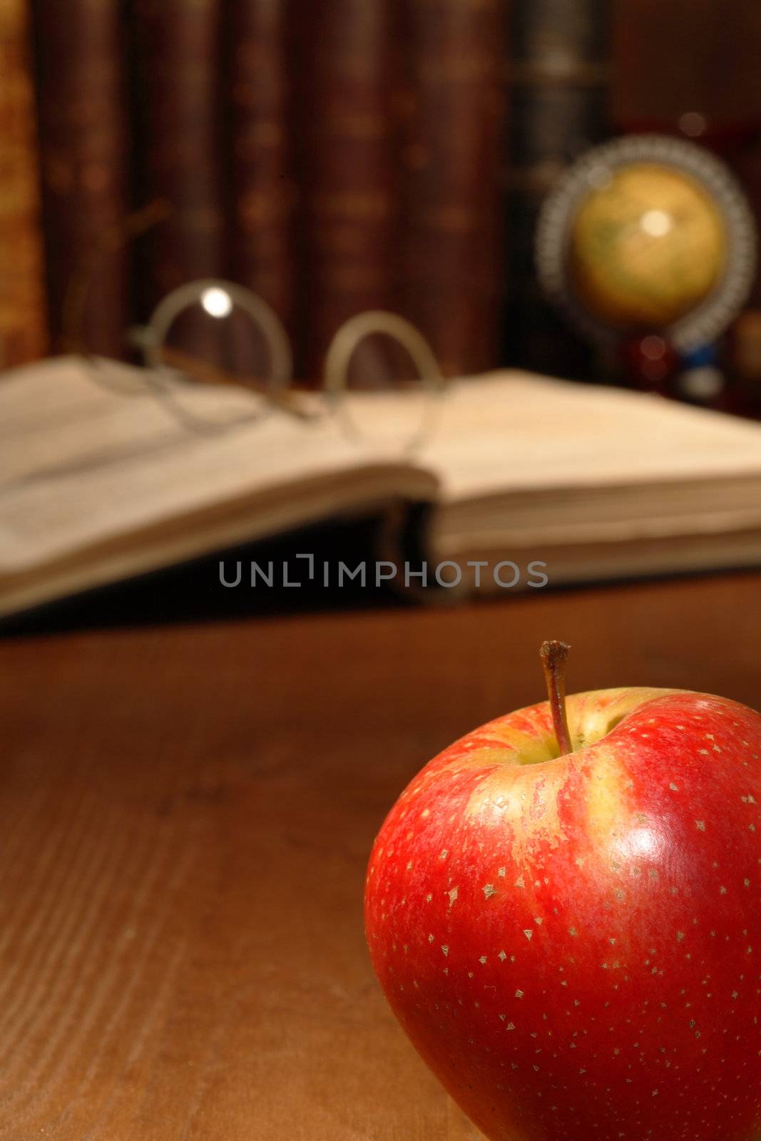 Closeup of red apple lying on wooden table with old books and spectacles