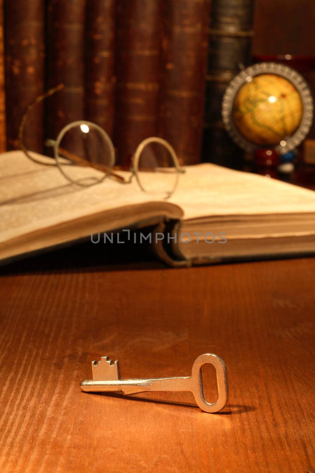 Old key lying on wooden background with books and spectacles