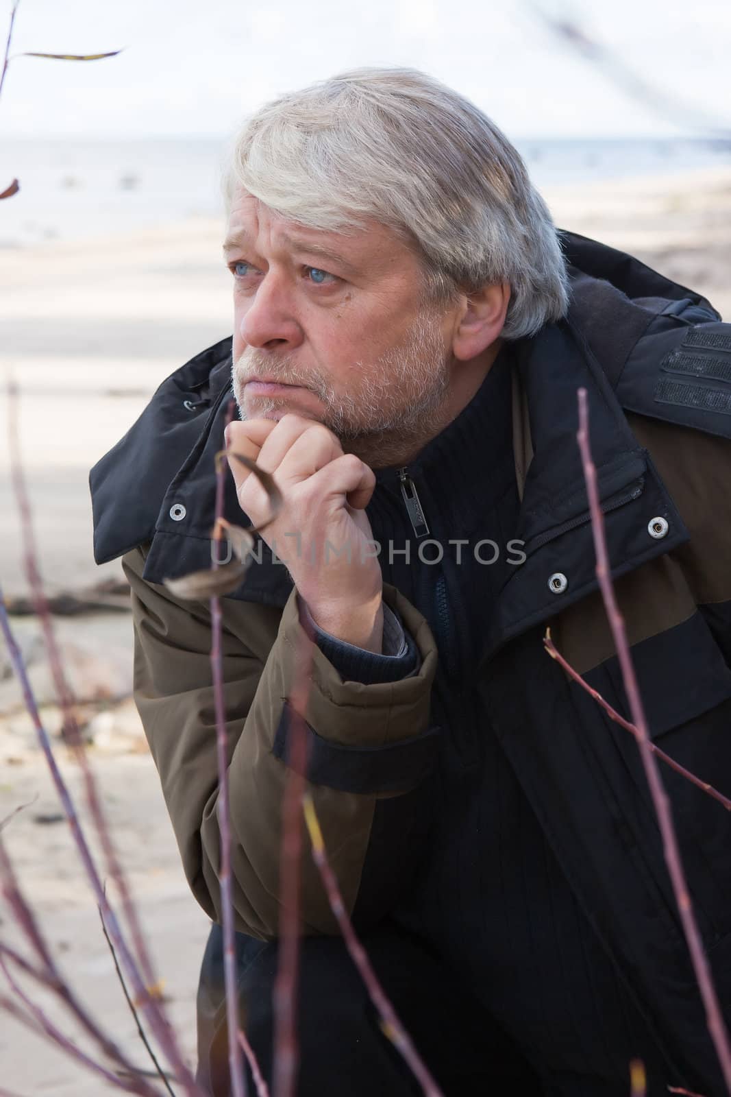 Portrait of mature thoughtful man with grey hair at the Baltic sea in autumn day.