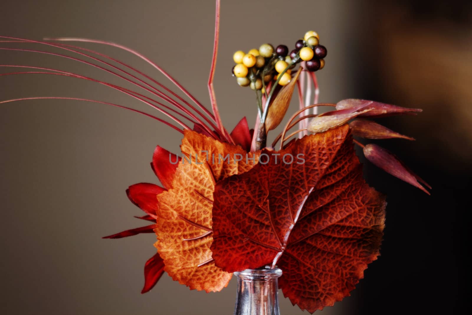 Auburn and orange leaves with berries in a small, tabletop vase capture the beauty of the season 