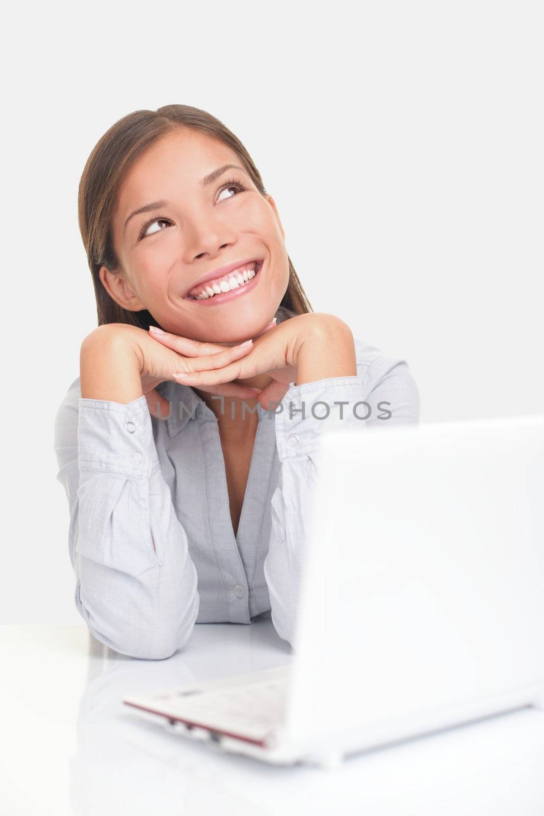 Woman thinking happy looking up at copy space while sitting at desk in front of laptop.