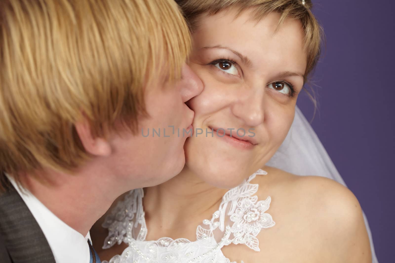 The groom kisses the bride on a purple background