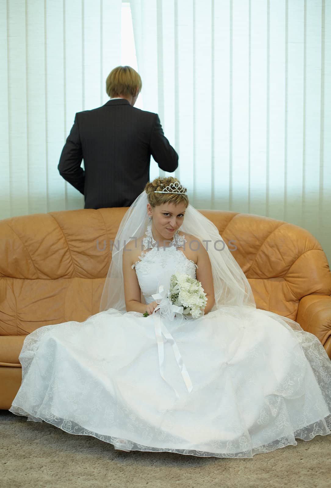 Bride sitting on couch, groom looks out window by pzaxe