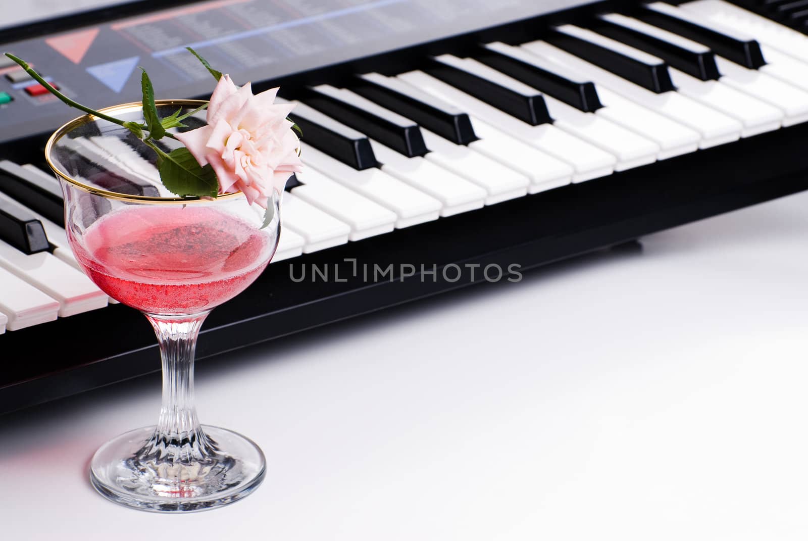 An electronic keyboard along with a fresh rose and a glass of pink wine, shot on white