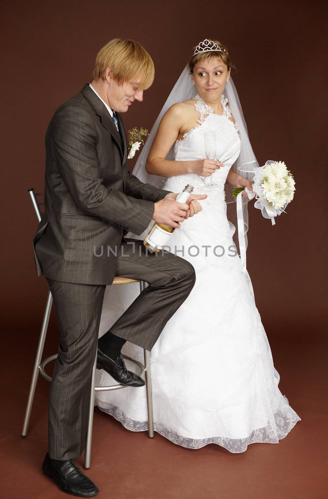 Bridegroom opens champagne wine on a brown background