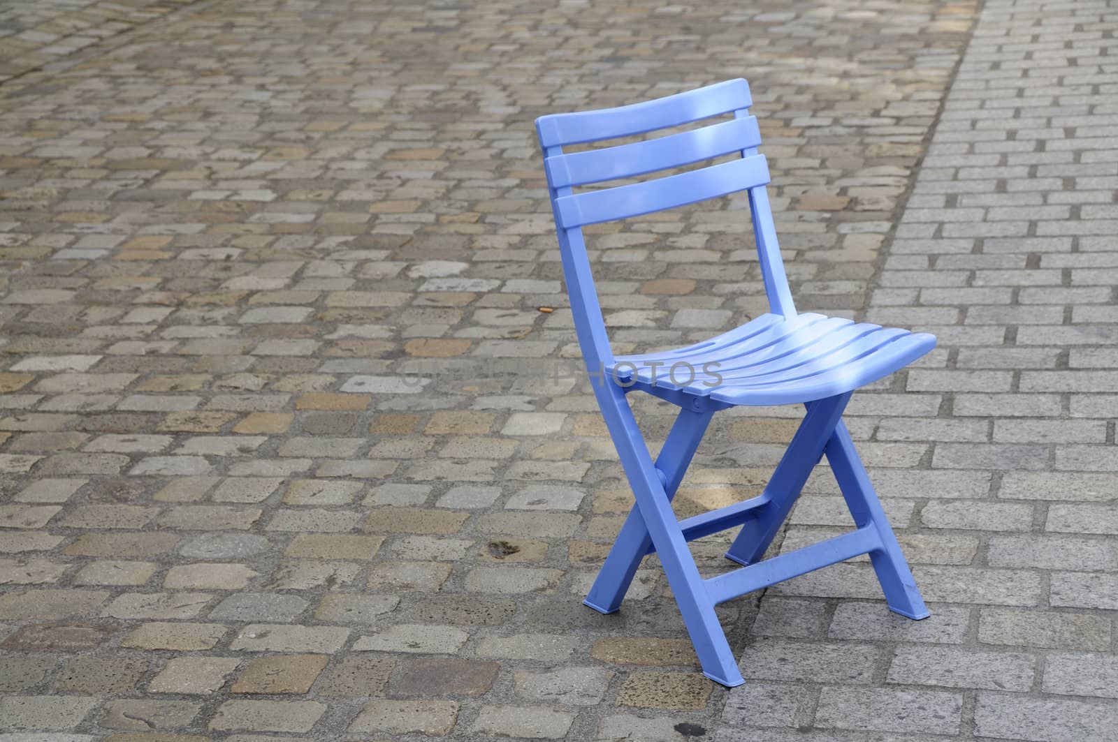 Shot of blue folding chair on cobbled pavement