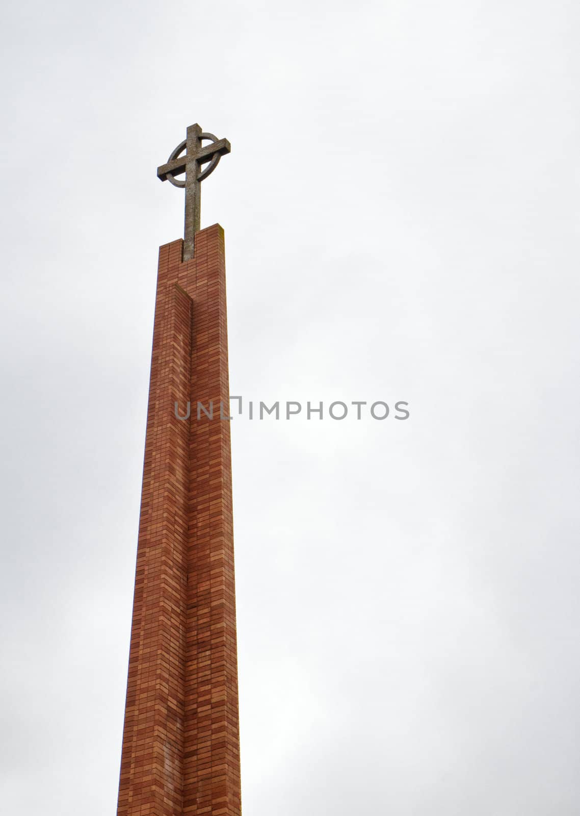 Church cross on top of a red brick tower against a cloudy sky