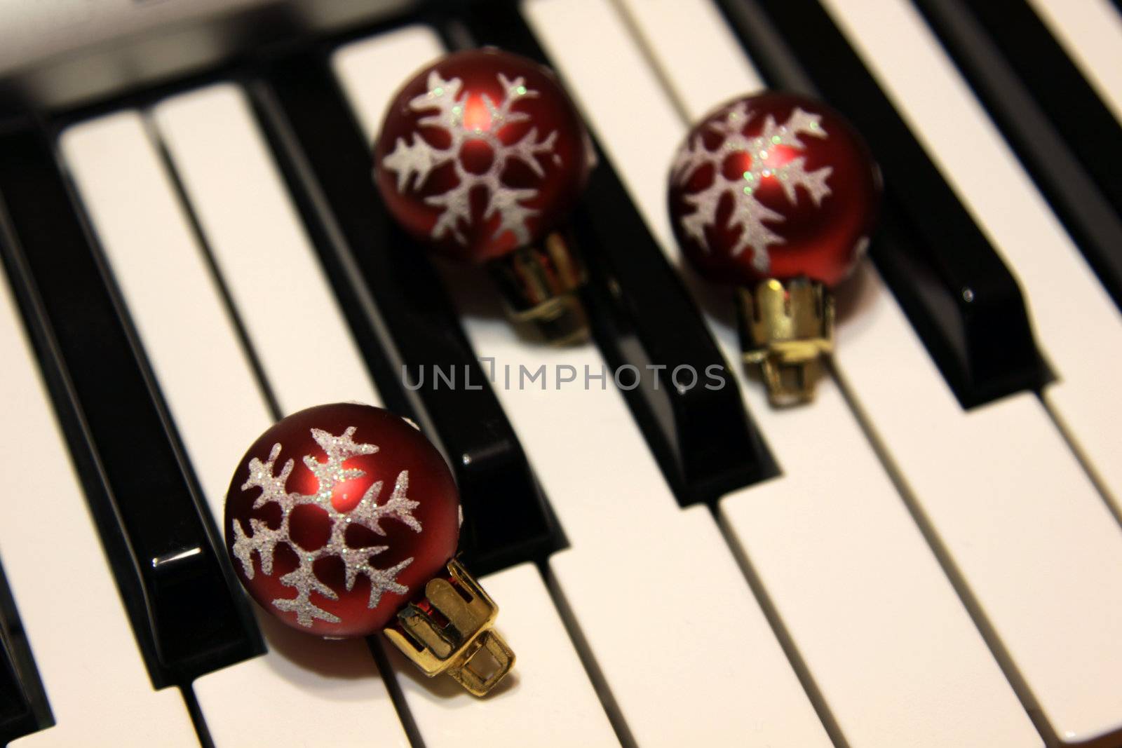 Three red snowflake Christmas baubles sitting on piano keys.
