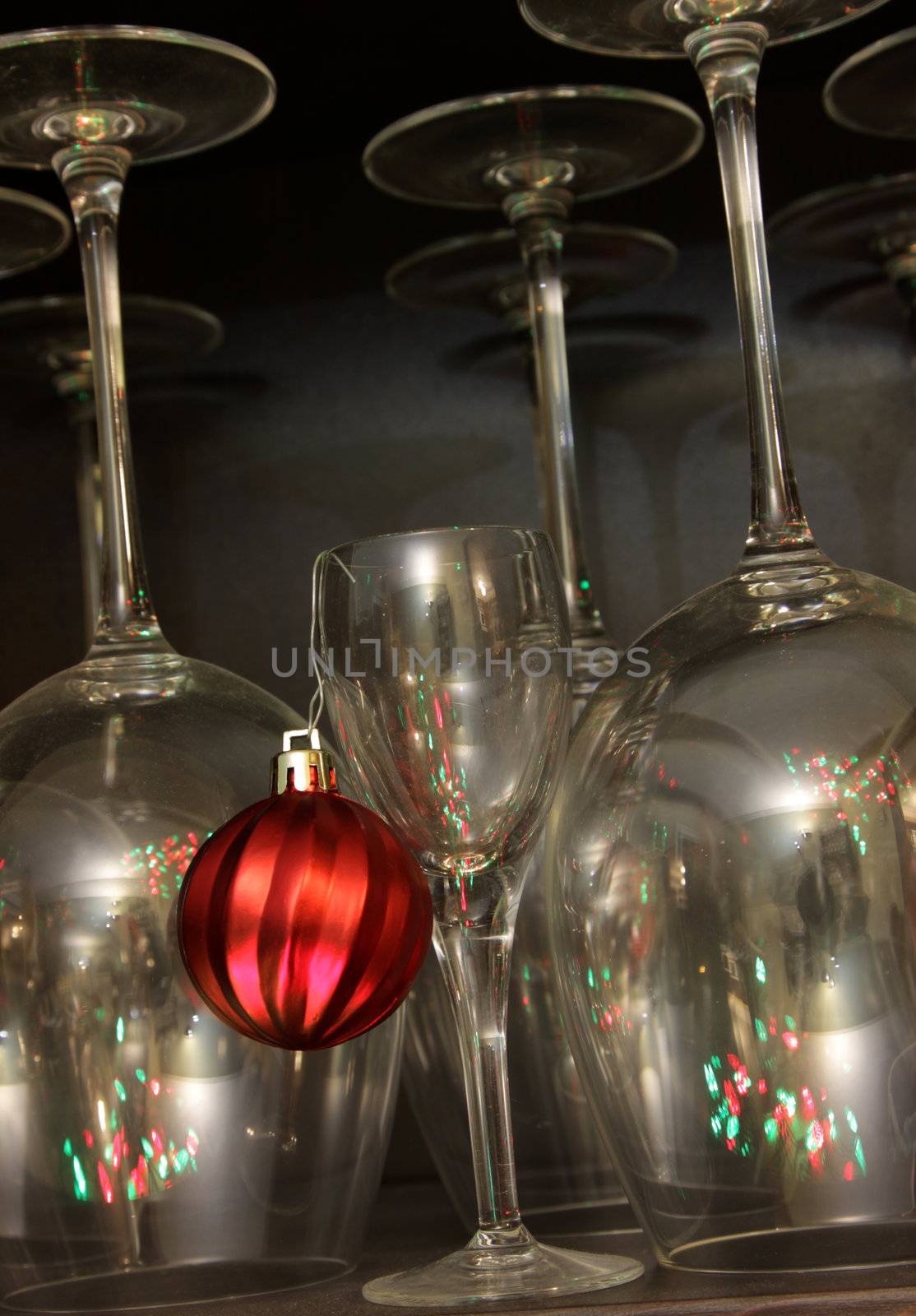 A red Christmas bauble ornament hanging from a dessert glass with wine glasses in the background.
