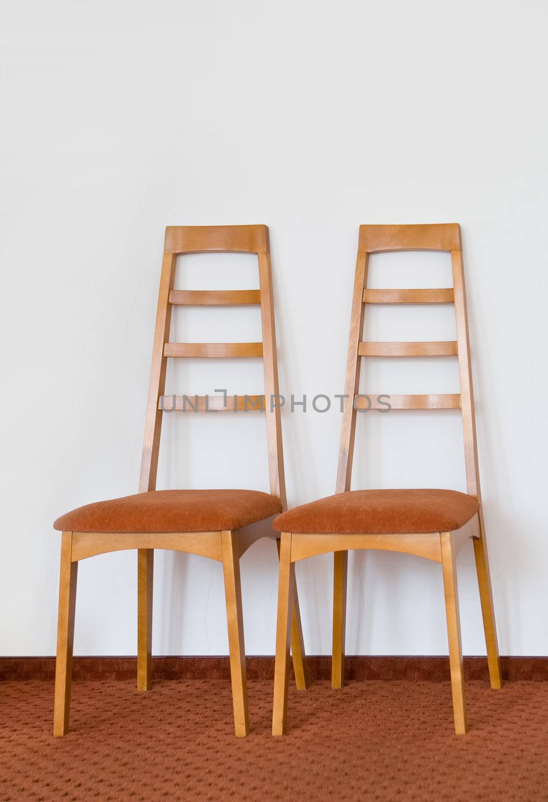 Two modern wooden chair. White wall and brown floor