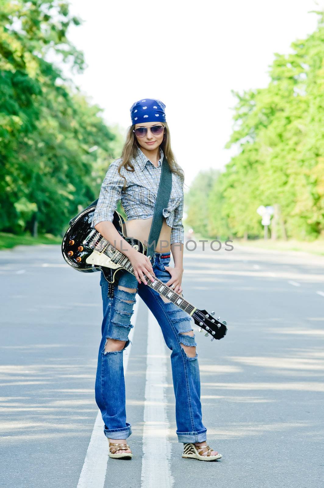 Rocking girl on a highway road with guitar