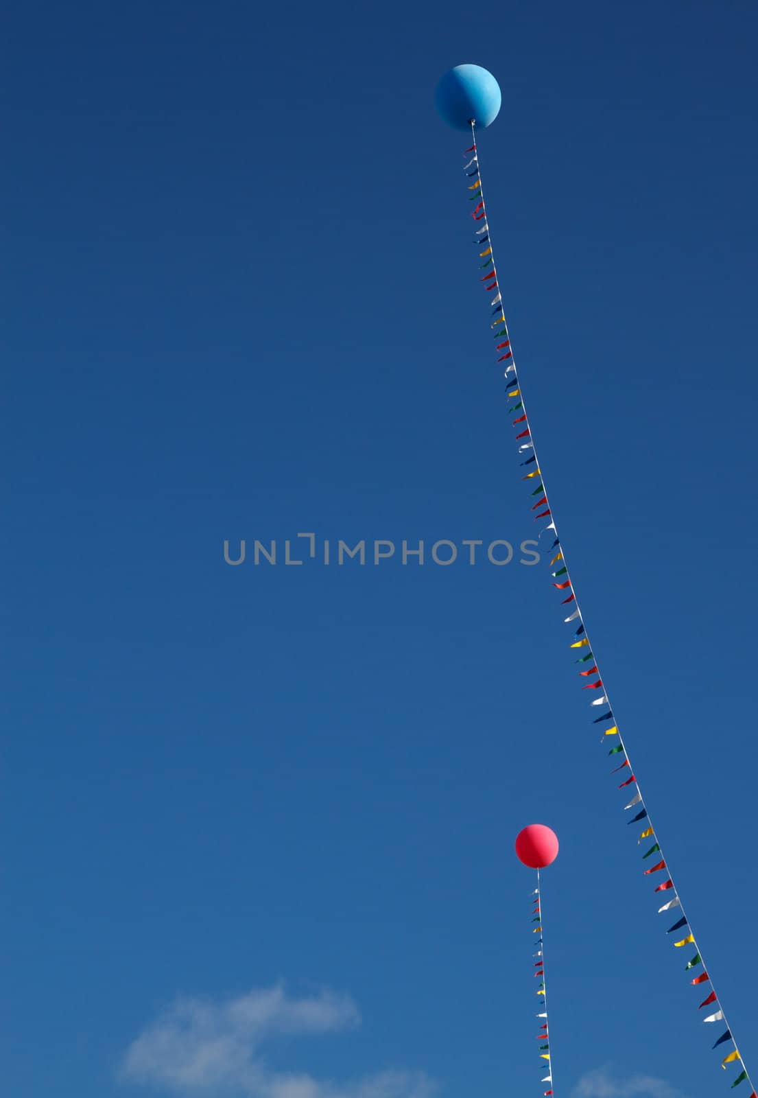 Two  helium balloons, one red and one blue, held in place by a flagged line against a blue sky