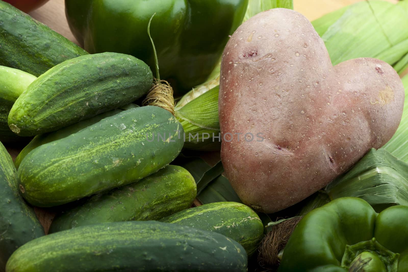 a heart shaped potato laying on corn cucumbers and green peppers