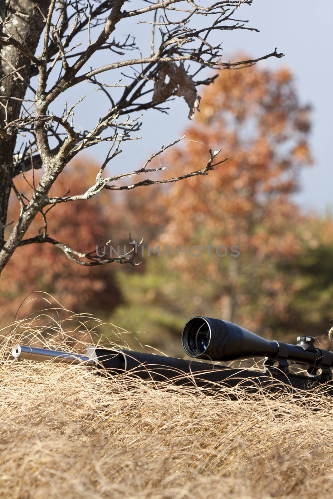 sniper laying on the ground covered in a ghille suite tall grass and trees in the background