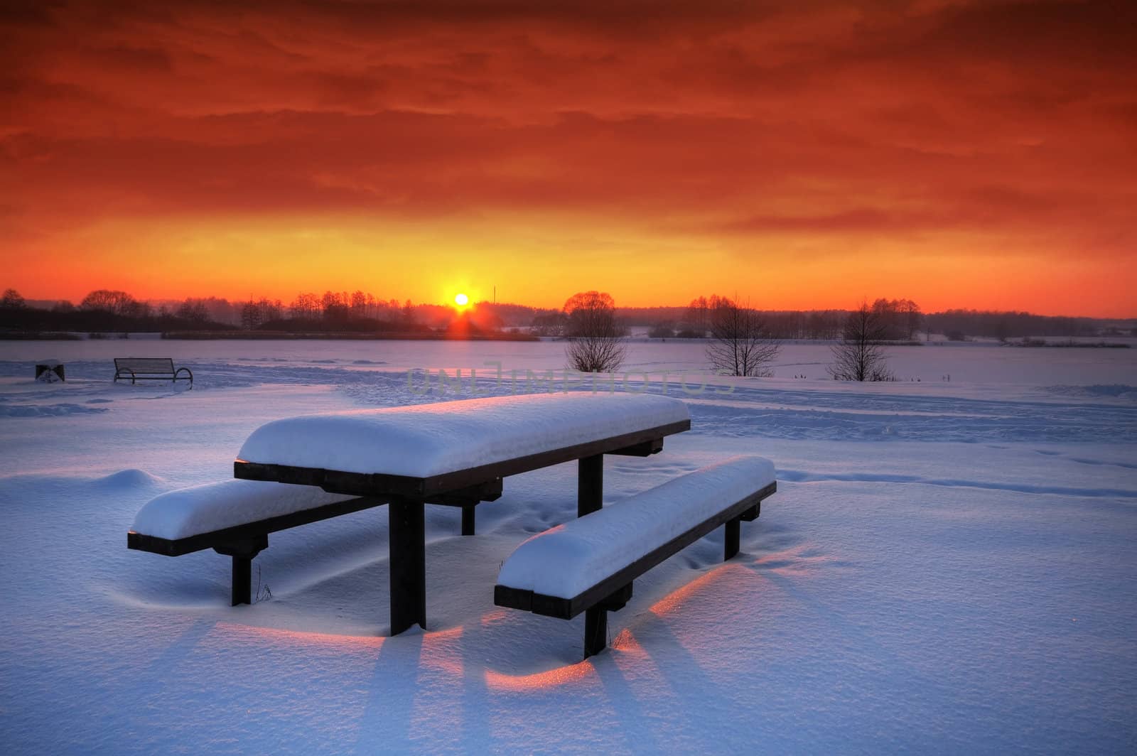 Spectacular winter sunset with a table and benches covered with snow