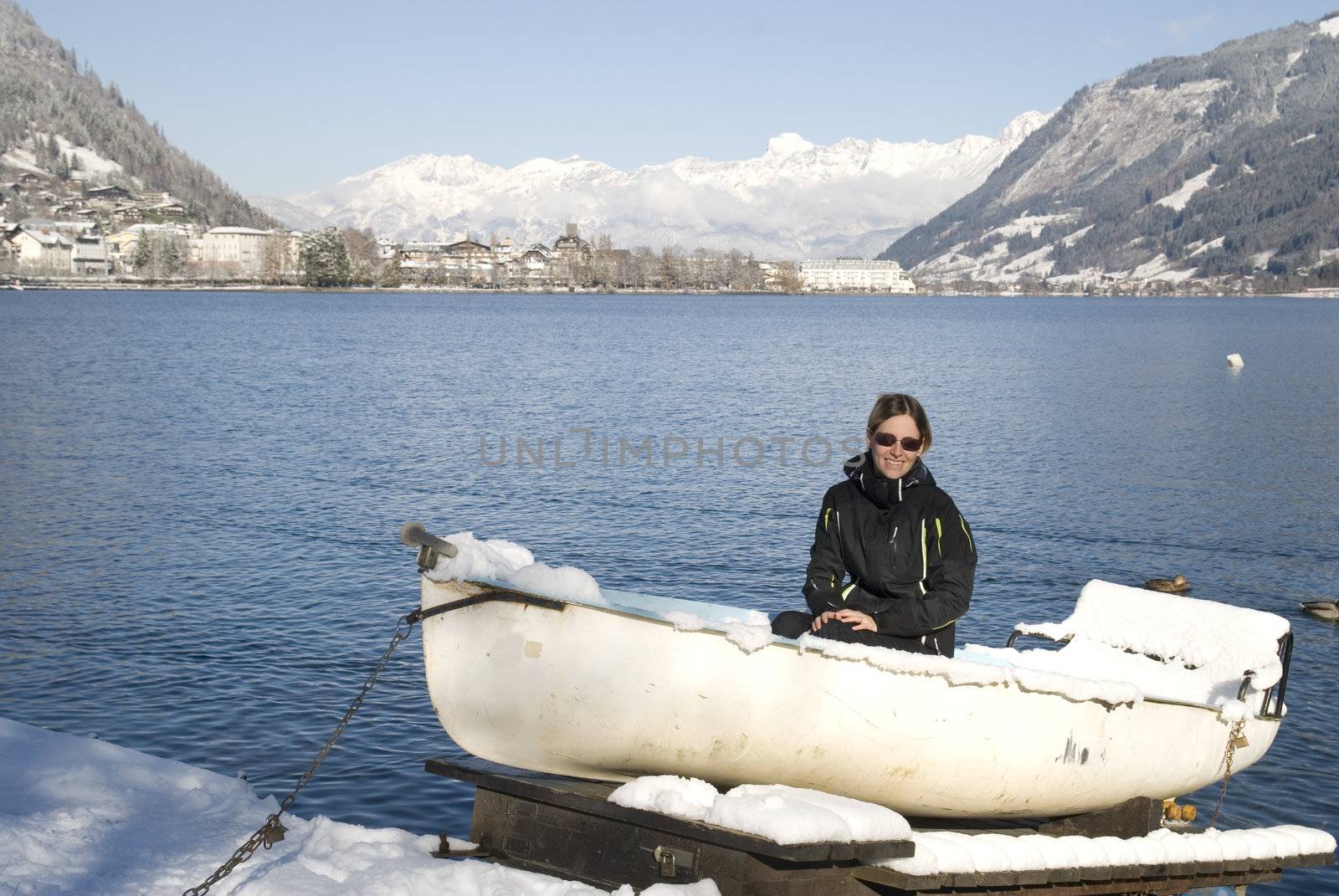 Shot of young woman sitting in snow covered boat at the lake of Zell am See in Austria.