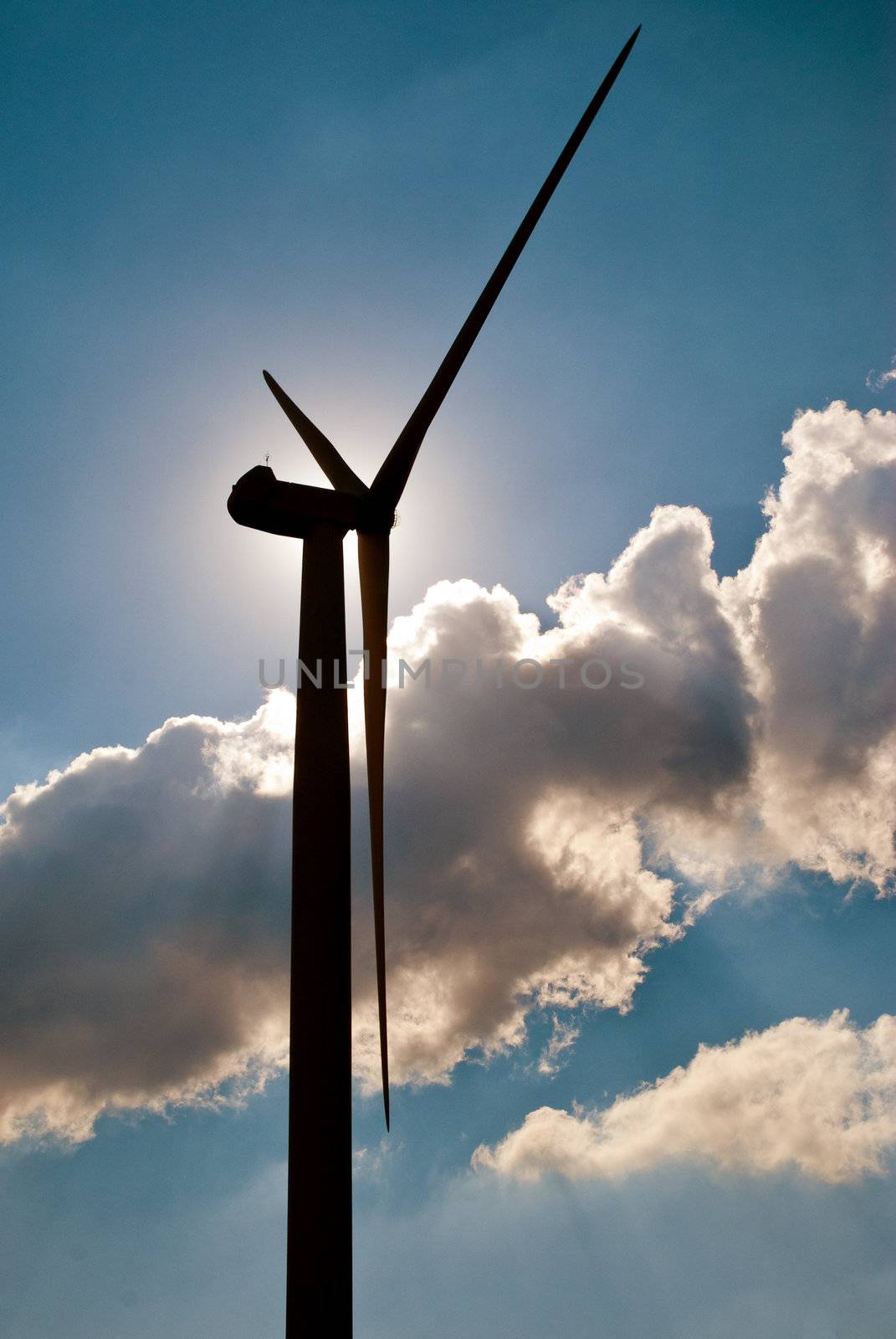 Wind turbine in the back light of the sun with blue sky and clouds.