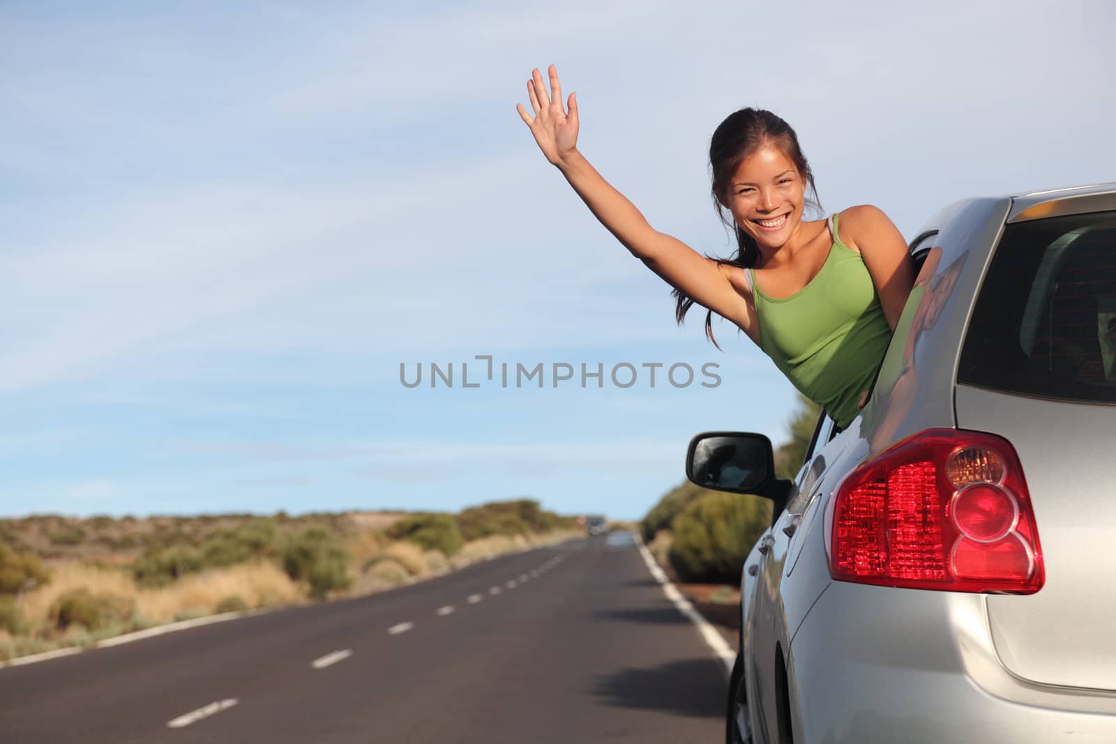 Woman in car road trip waving out the window smiling.  Image from Teide, Tenerife. Mixed race Asian / Caucasian woman.