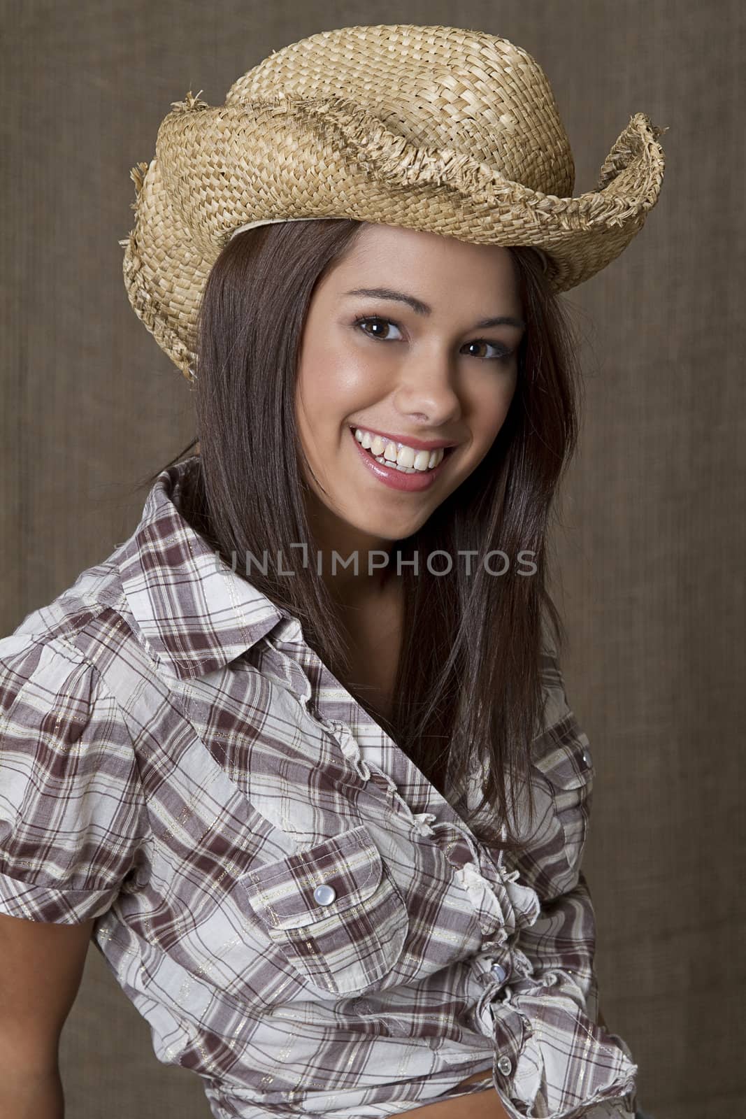 portrait of a young brunette cowgirl against a brown background