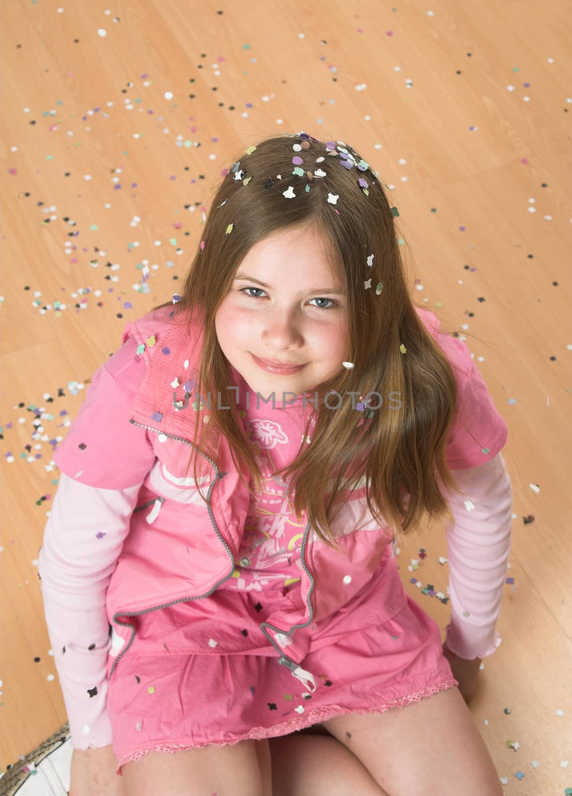 Little blond girl sitting on the floor covered in confetti