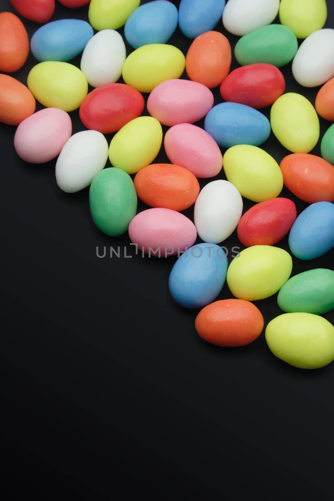 Very colourful sweets on a black surface. The candies are egg-shaped, but that should not limit the use to easter-topics only.