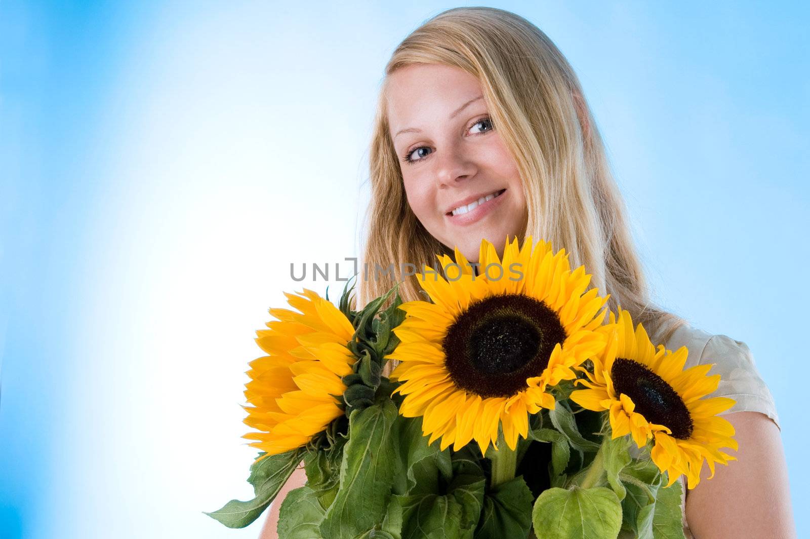 The attractive blonde in studio holds a sunflower in hands.