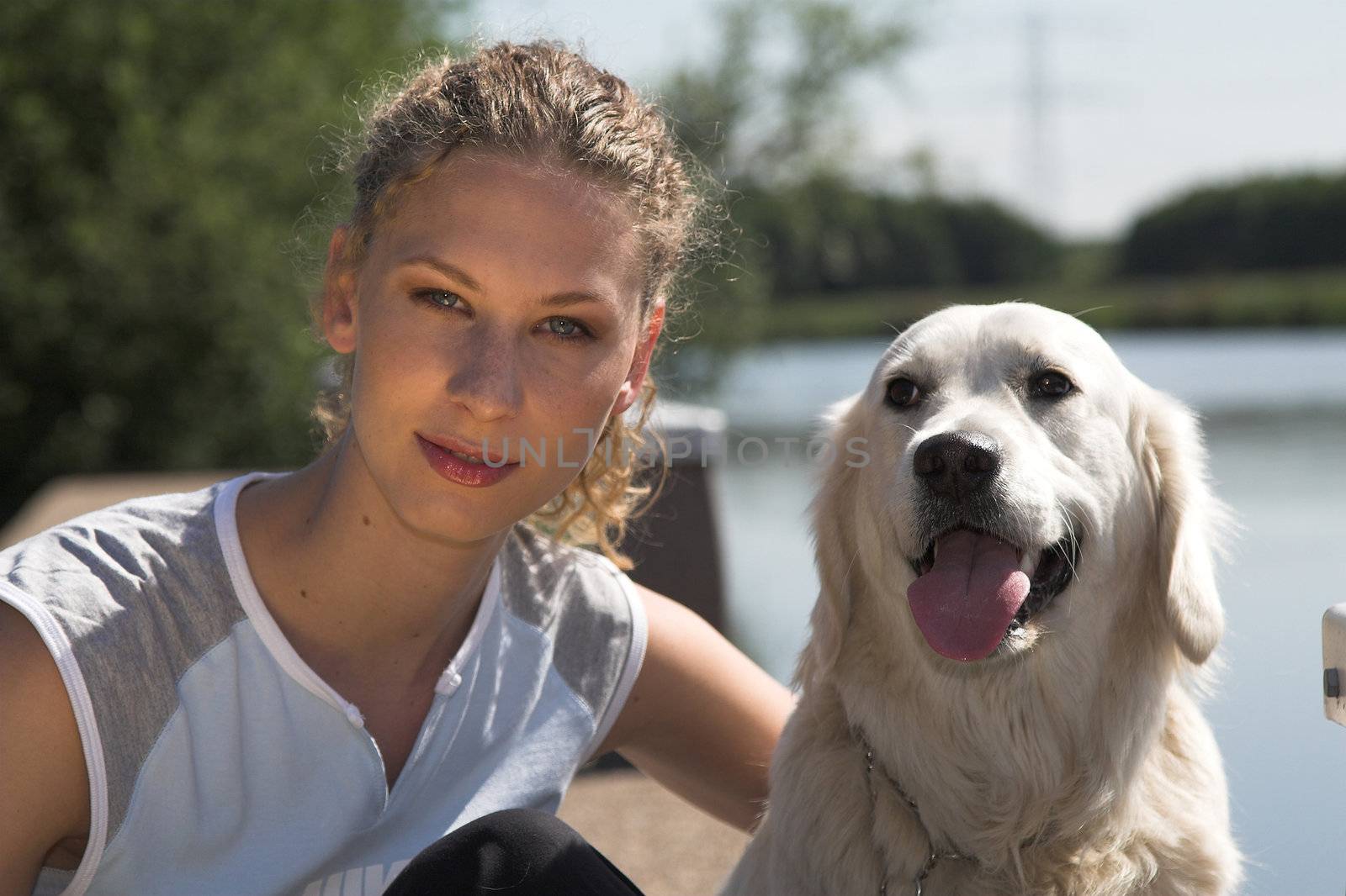 Beautiful curly blond woman sitting with her dog by the waterside