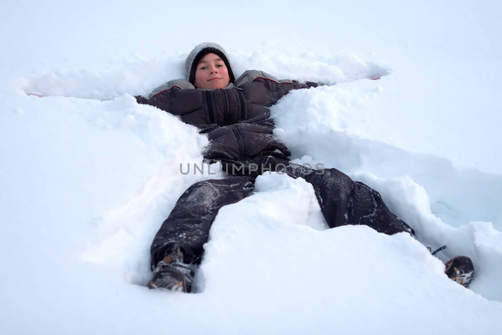 A happy young boy lays in fresh snow as he plays outdoors on a cold winter day.