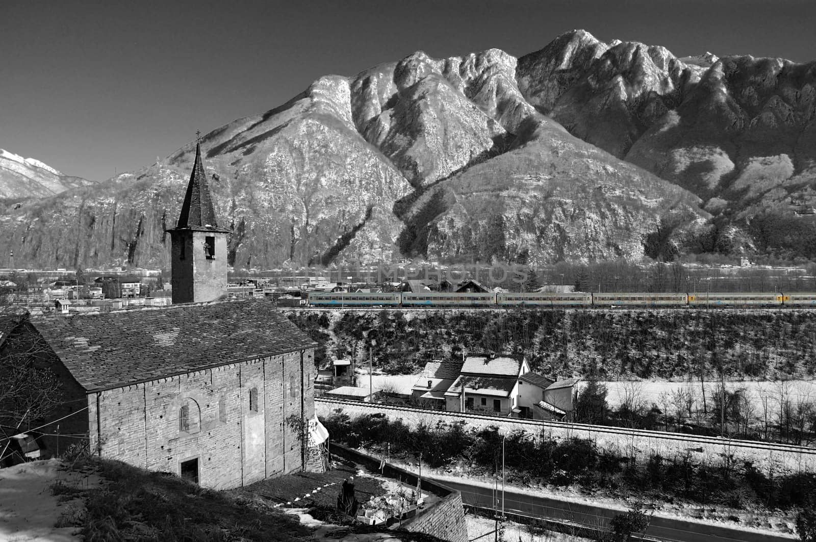 black and white view on Alpine S.Quirico Church in winter, Ossola valley and mountains in background, Domodossola, Italy