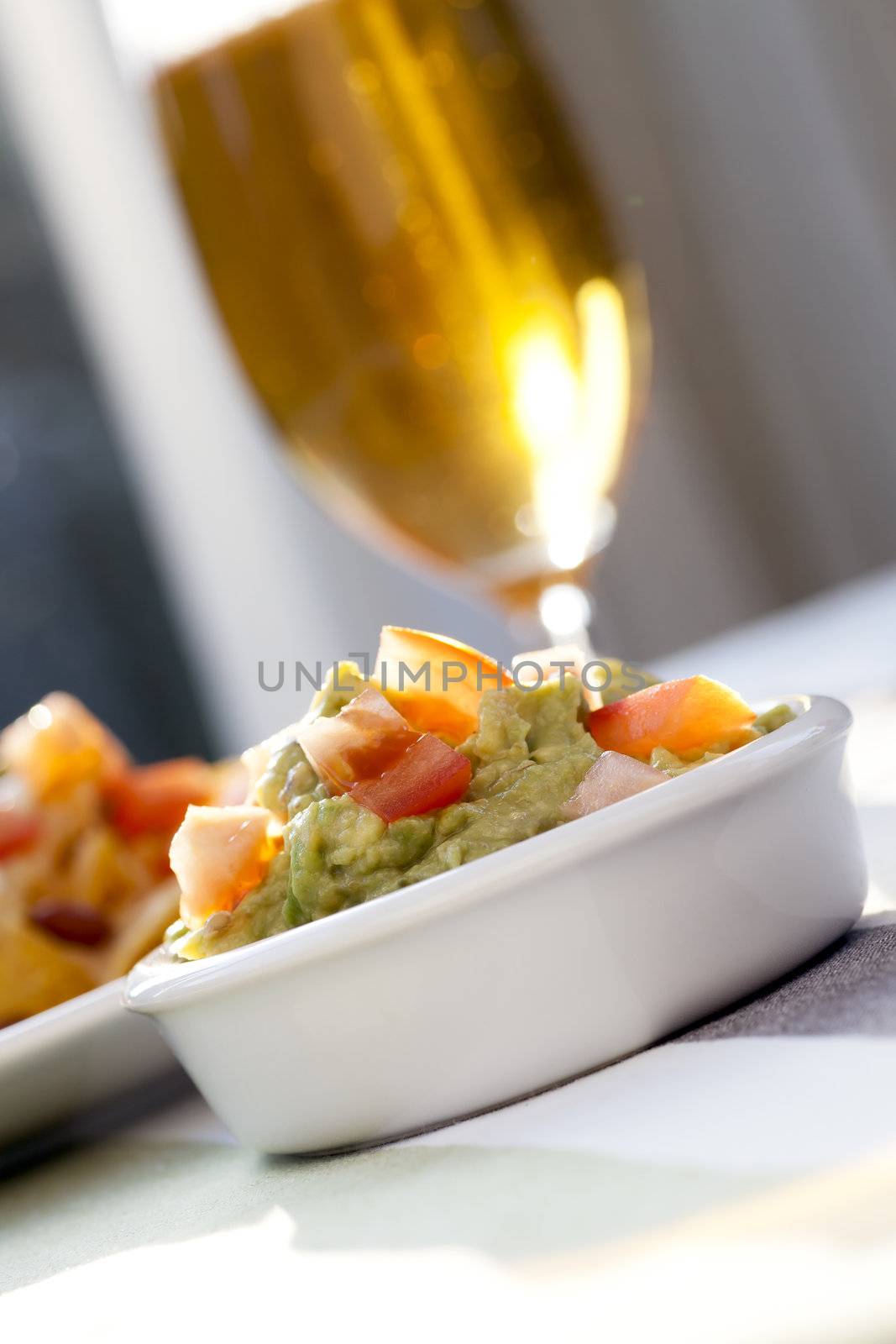 Guacamole dip with beer in background in sunlight.