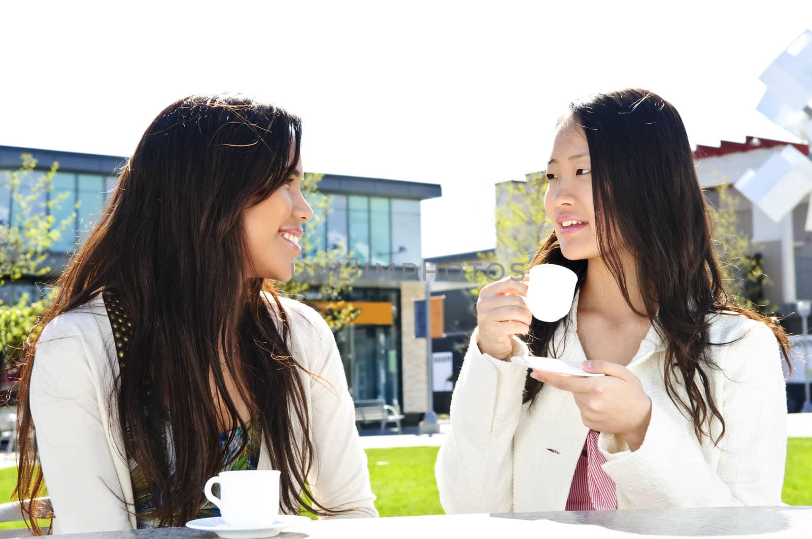 Two girl friends sitting and having drinks at outdoor mall