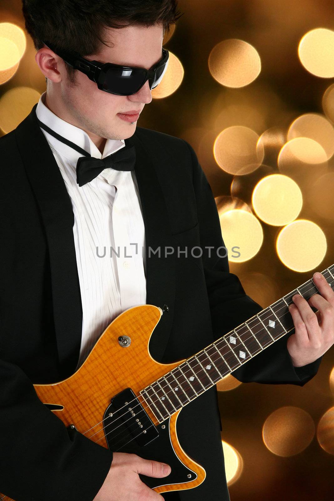 Attractive young man teenager  in tux with electric guitar over defocused lights.