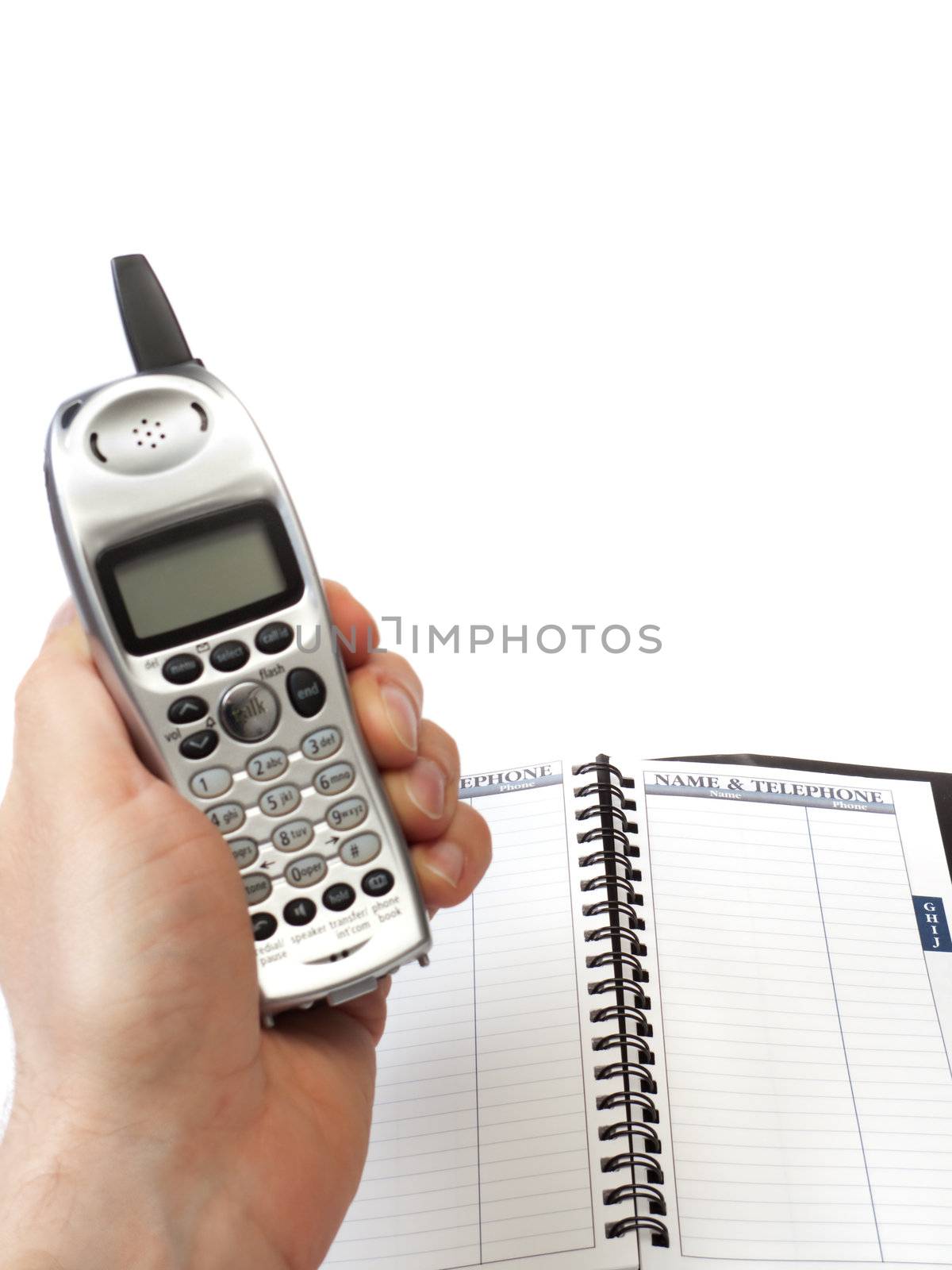 A hand holding a cordless phone, with the display facing the camera, and a blank telephone directory, isolated on white.