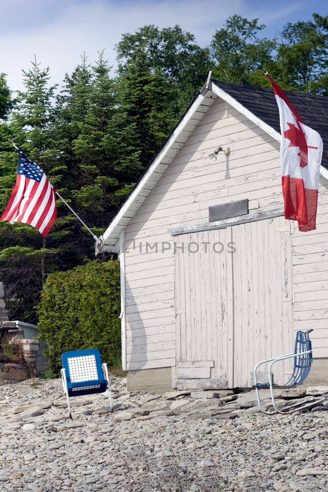 An old boathouse with American and Canadian flags on either side, with two chairs in front.  On the shores of Georgian Bay, in the Bruce Peninsula.