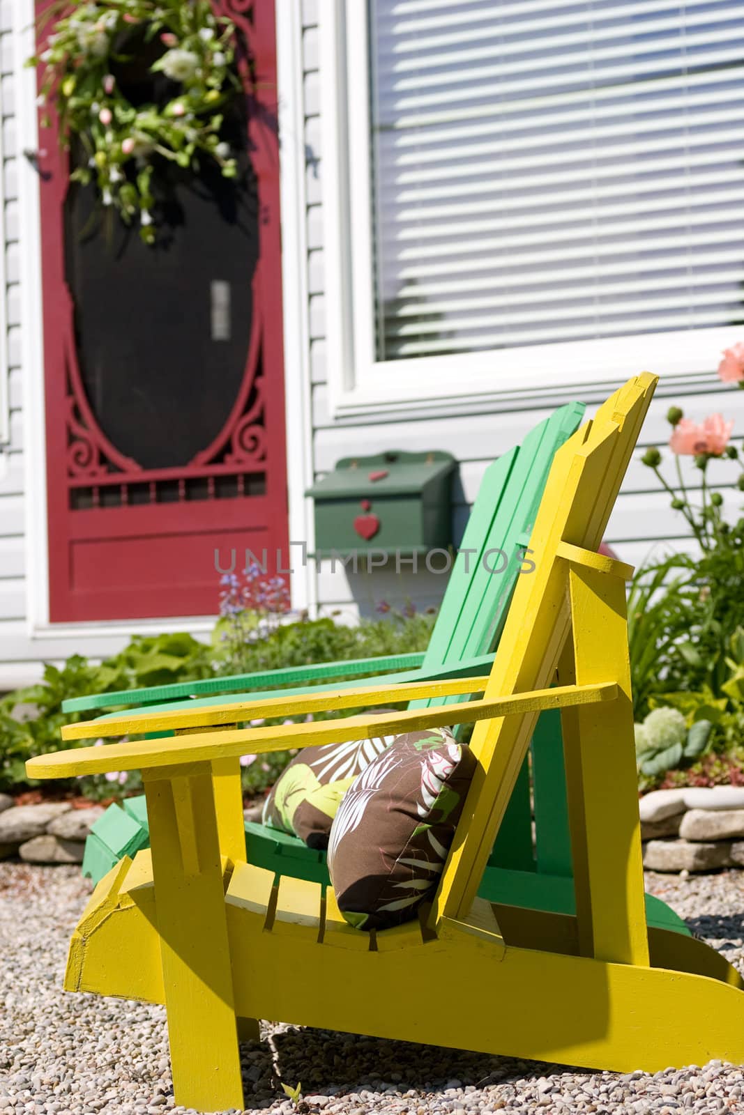 The front of a cottage with two brightly colored adirondack chairs and an equally colored front door.