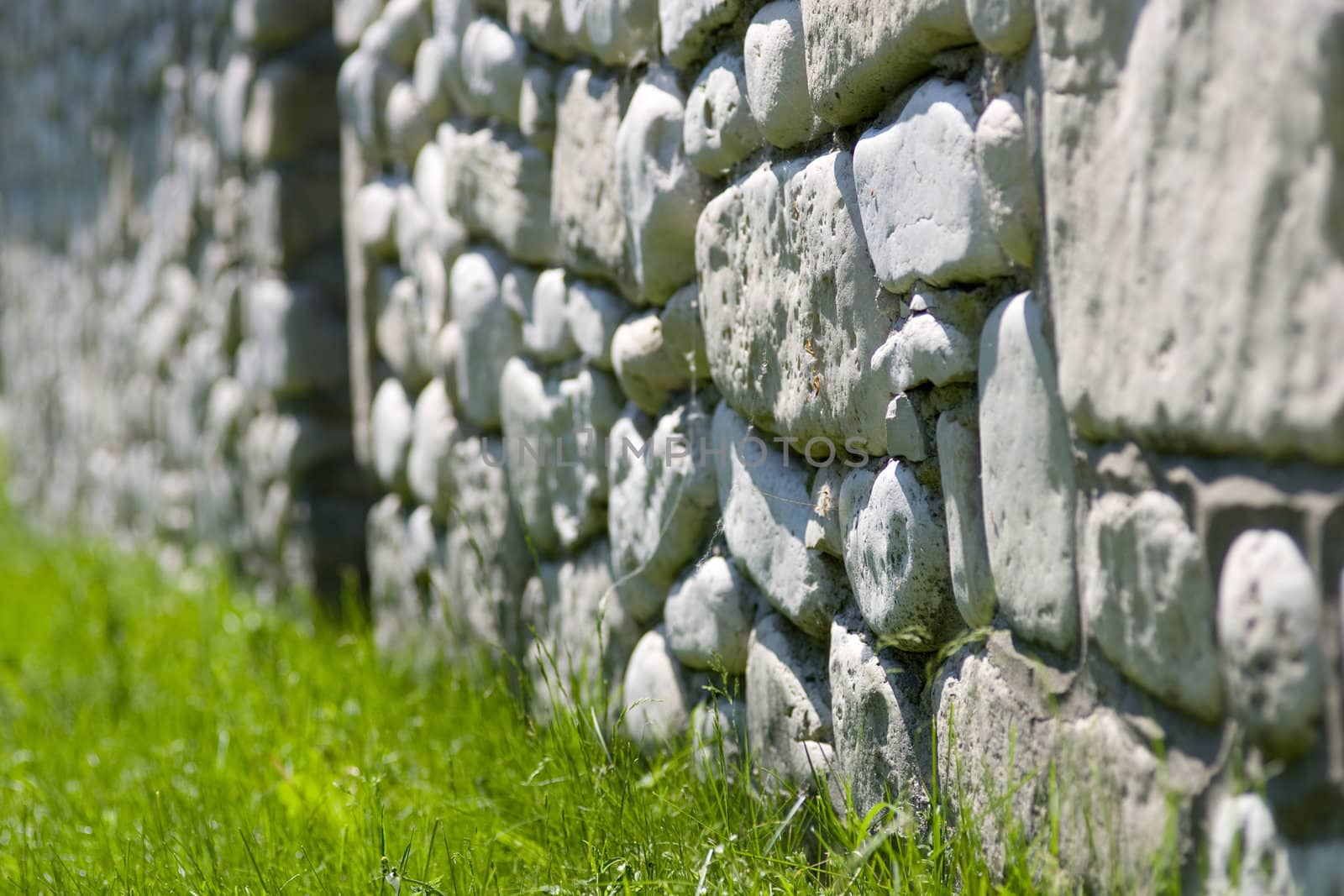 An old wall made out of local shore stone, against a carpet of green grass.