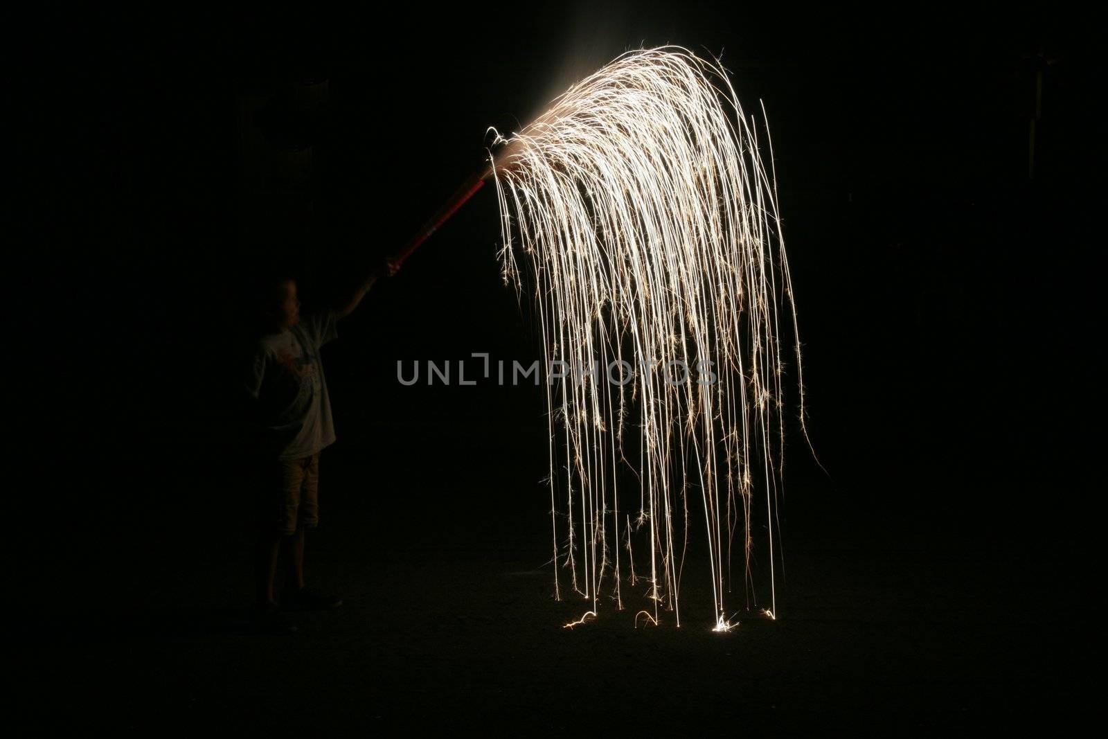 Young boy illuminated by fireworks spouting out of the fountain he was holding